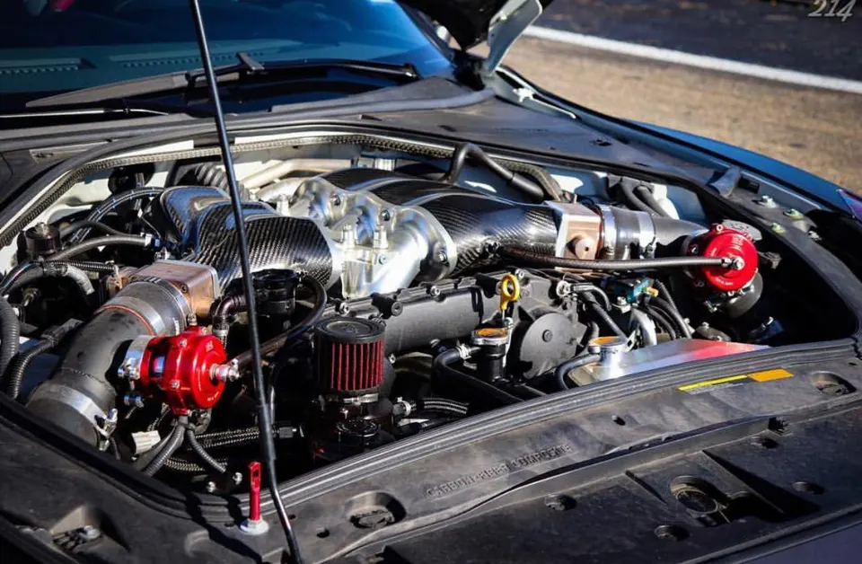 Close-up of a modified Nissan GT-R engine bay featuring a carbon fiber intake manifold and red blow-off valves.