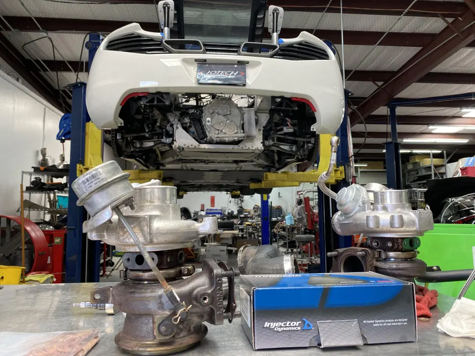White McLaren on a lift in a performance shop with turbochargers and Injector Dynamics fuel injectors on a workbench.