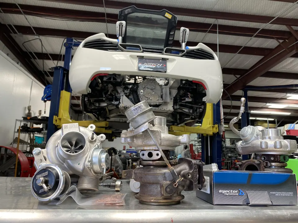 A white McLaren on a lift in a performance shop, with new and old turbochargers and fuel injectors on a table.