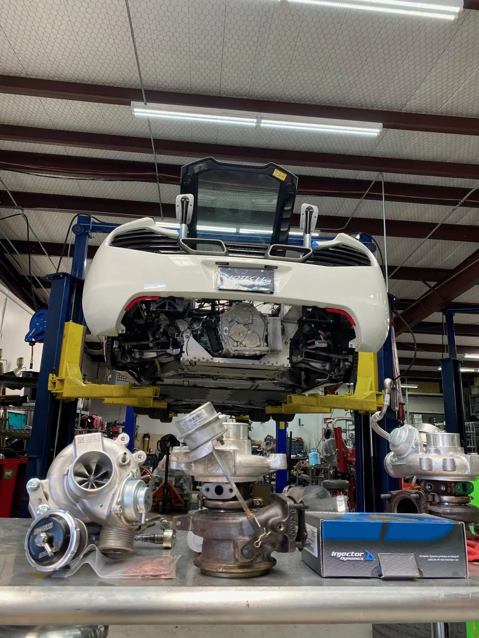 McLaren on a lift in a performance shop with new turbochargers and fuel injectors on a workbench.