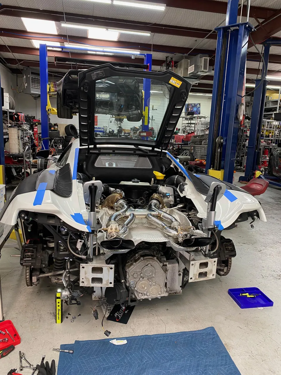 A McLaren supercar with its rear bodywork removed, showcasing an aftermarket turbocharger and exhaust system installation in a performance tuning shop.