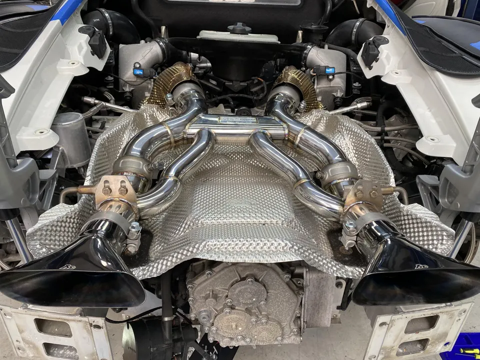 A detailed view of a McLaren's engine bay showcasing a custom performance exhaust system with heat shielding.