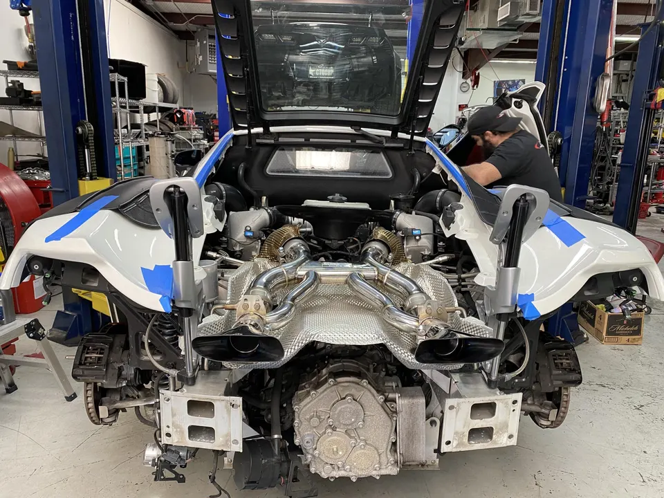 A McLaren supercar in a shop with its rear bodywork removed, revealing the twin-turbo engine and custom exhaust system.