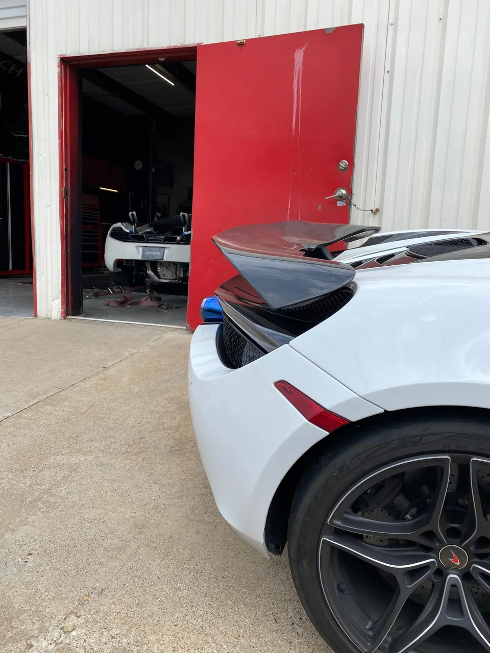 White McLaren with a carbon fiber active rear wing parked outside a Jotech Motorsports shop, with another McLaren inside.