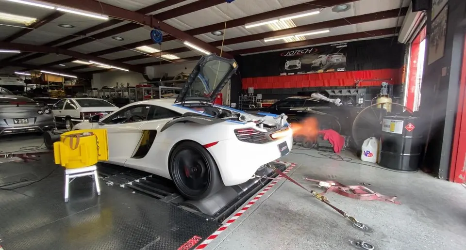 White McLaren on a dyno at Jotech Motorsports performance shop, with exhaust flames during a tuning session.