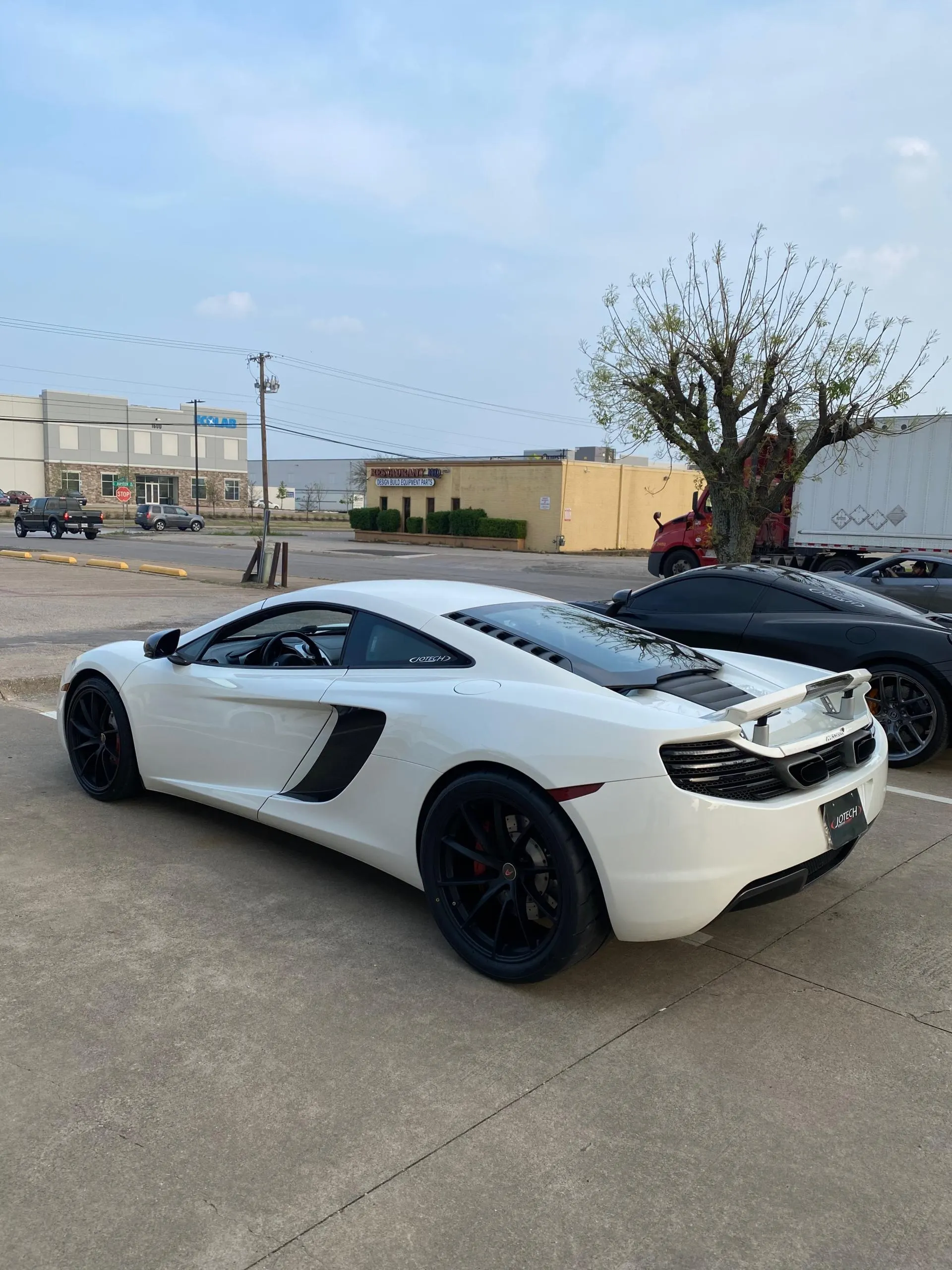 White McLaren 12C supercar with black wheels parked outdoors.