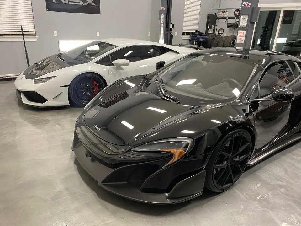 White Lamborghini Huracan and black McLaren supercar parked on a polished floor in a performance tuning shop.