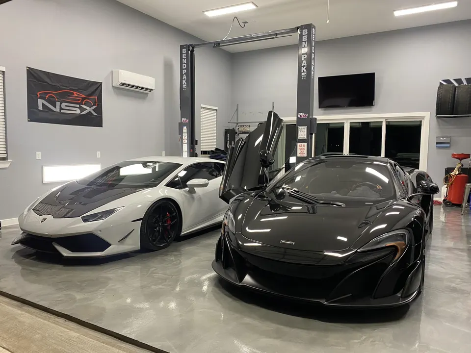 A white Lamborghini Huracan and a black McLaren supercar parked side-by-side in a clean performance shop garage.