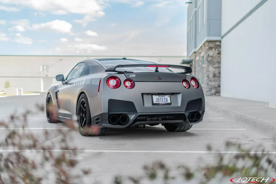 Rear view of a grey Nissan GT-R R35 with an aftermarket rear wing, diffuser, and quad exhaust tips, parked outdoors.