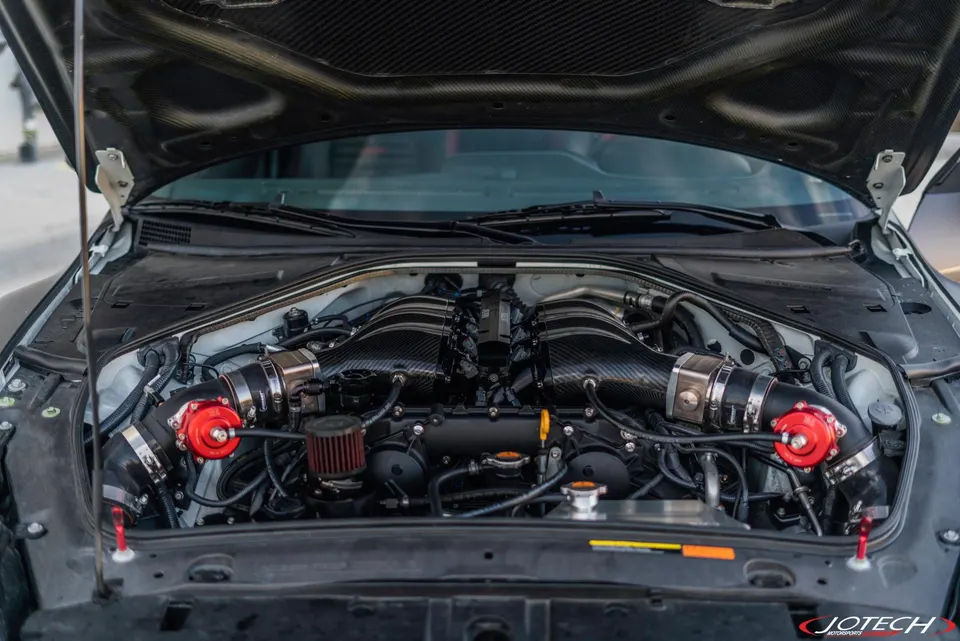 Close-up of a Nissan GT-R VR38DETT engine bay with carbon fiber intakes and red blow-off valves.