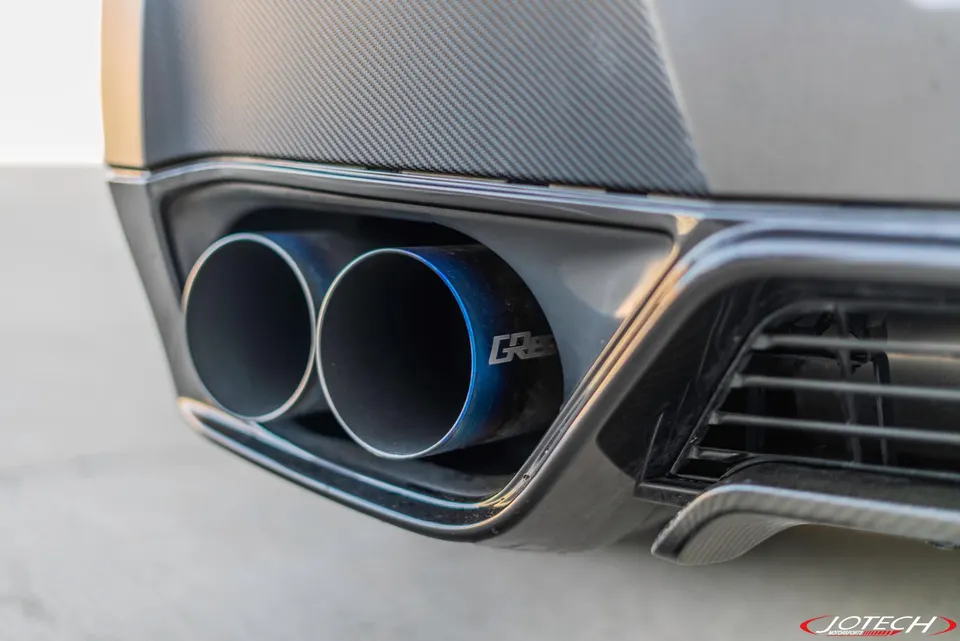 Close-up of blue titanium exhaust tips and a carbon fiber rear diffuser on a performance car, featuring the Jotech Motorsports logo.