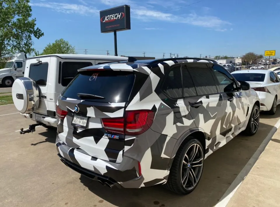 A BMW X5 M SUV with a black, white, and grey camouflage wrap parked outside Jotech Motorsports.