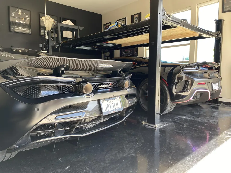 Two black McLarens, a 720S and a 600LT, parked in a garage with a car lift, highlighting carbon fiber aero.