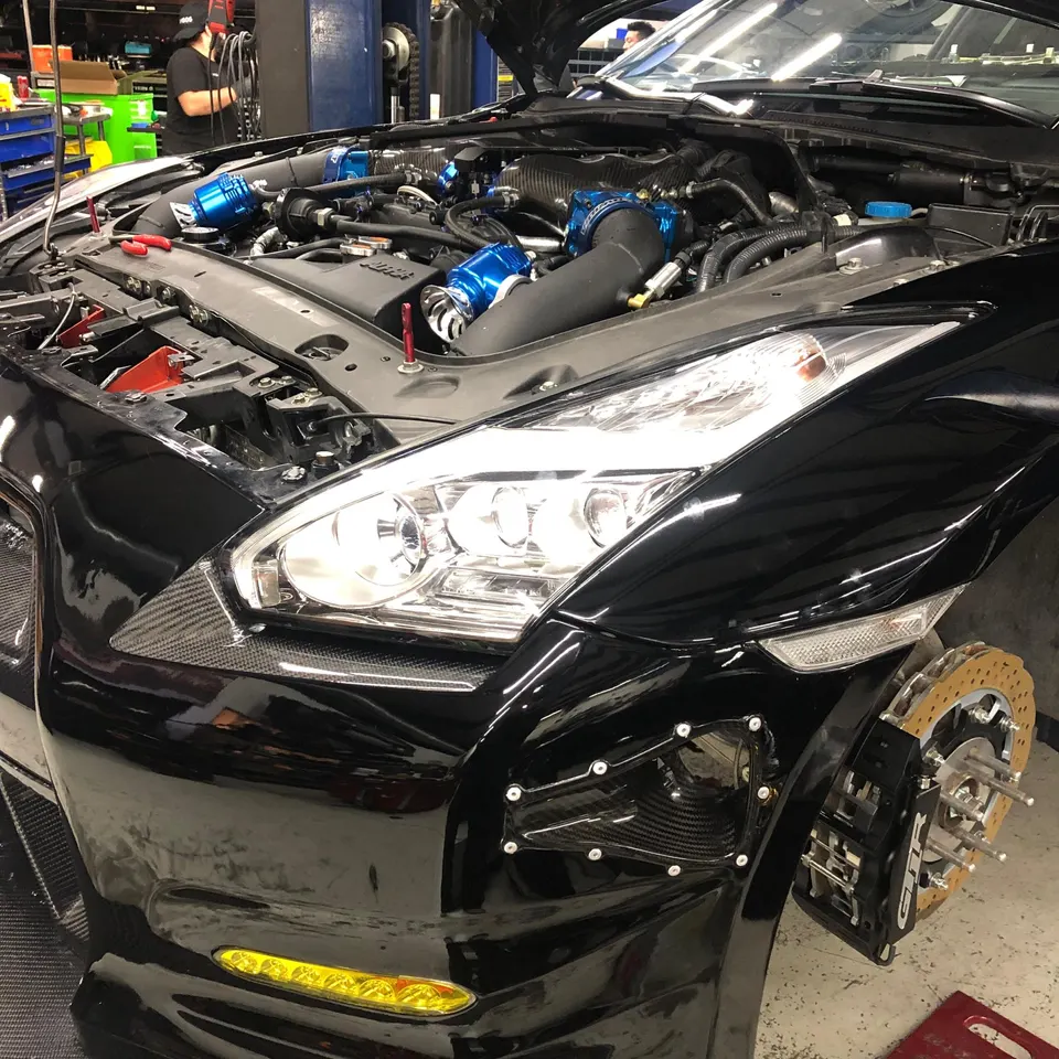 A black Nissan GT-R with its hood open in a shop, showcasing aftermarket engine components and large performance brakes.