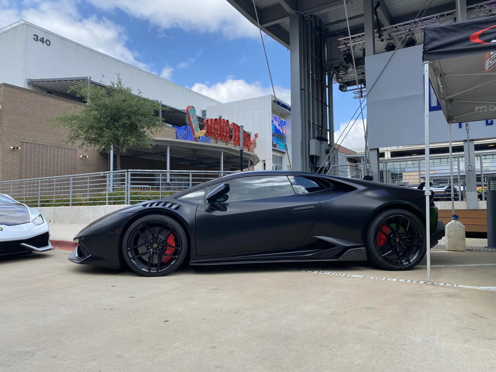 Matte black Lamborghini Huracan supercar parked at an outdoor car show or event with red brake calipers.