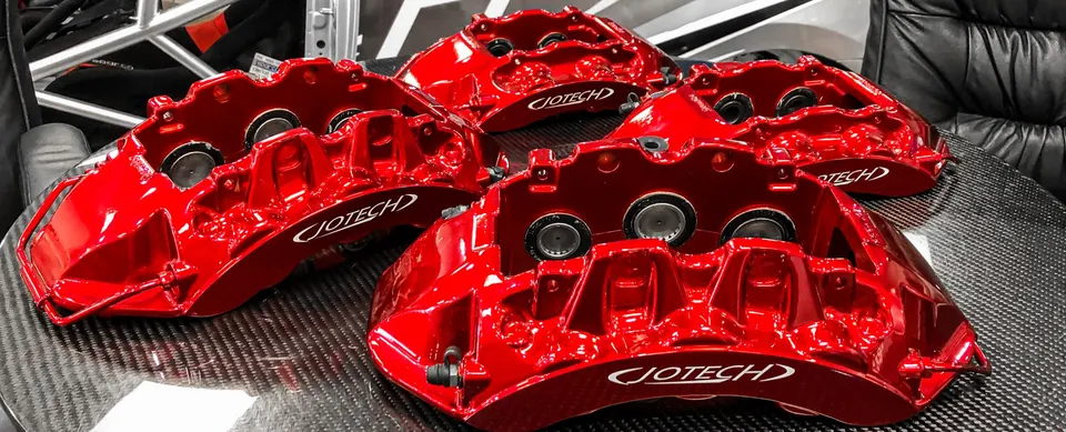 Red Jotech performance brake calipers displayed on a carbon fiber surface, ready for installation on a high-performance vehicle.