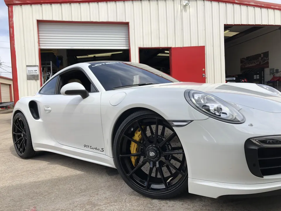 White Porsche 911 Turbo S with black wheels and yellow brake calipers parked outside a Jotech Motorsports shop.