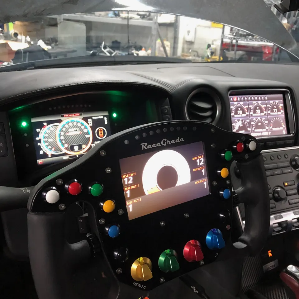 A custom RaceGrade steering wheel with an integrated digital display and multiple colored buttons in a performance car interior.