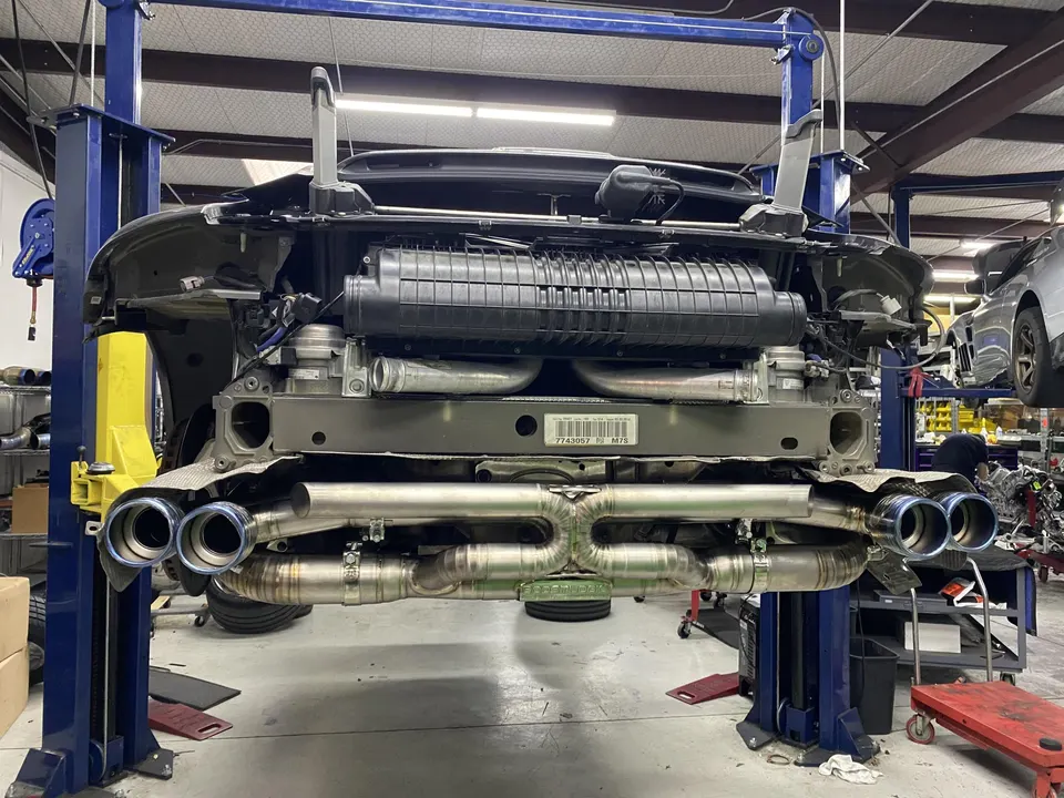 A Porsche 911 on a lift in a shop, showcasing an aftermarket exhaust system installation.