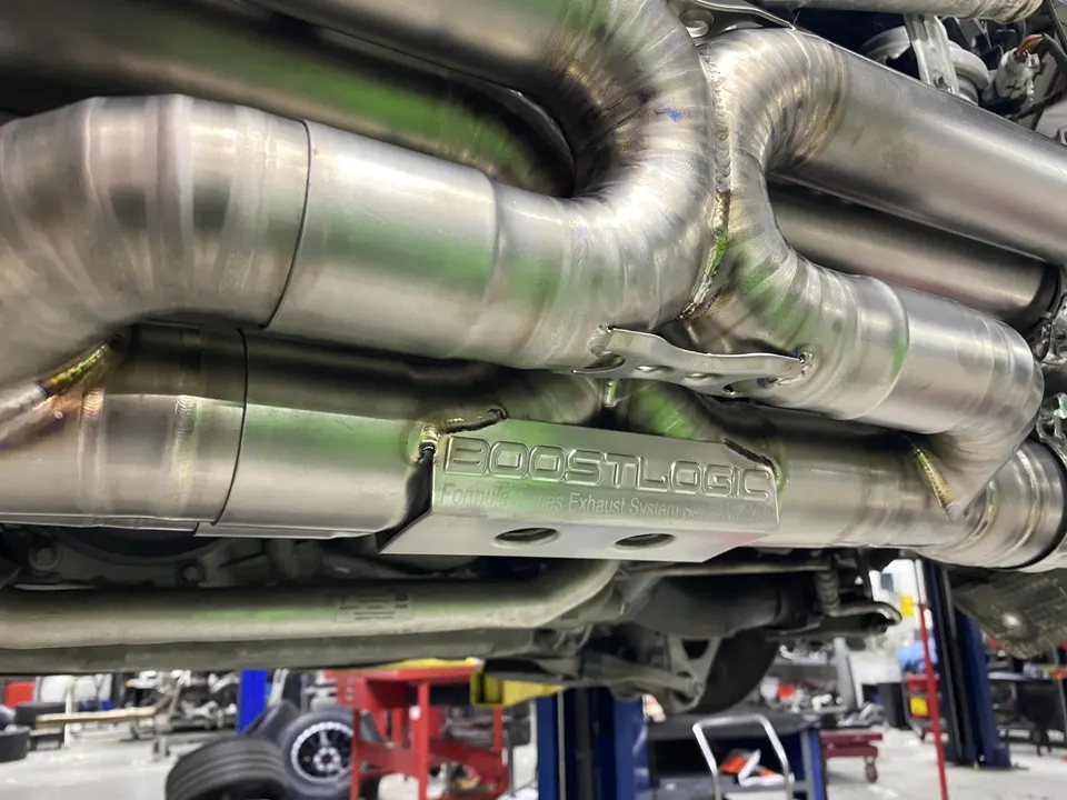 Boost Logic titanium exhaust system installed on the underside of a performance car in a shop.