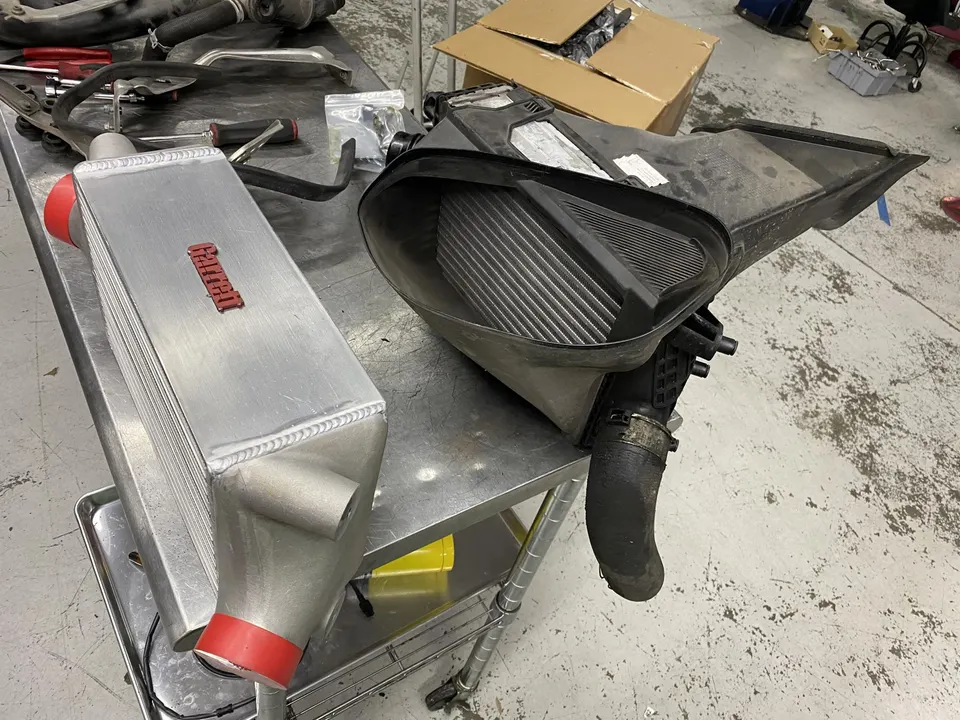 Garrett intercooler and OEM airbox on a metal workbench in a performance tuning shop, ready for installation.