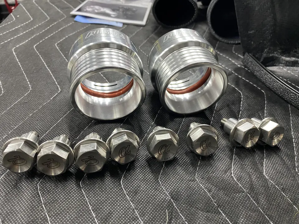 Alpha Performance boost pipe couplers and bolts laid out on a workbench, ready for installation in a performance vehicle.
