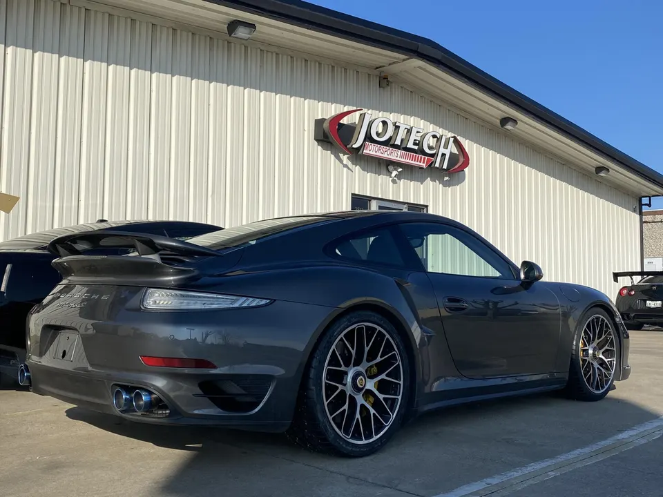 Grey Porsche 911 Turbo S with aftermarket wheels parked outside Jotech Motorsports performance tuning shop.