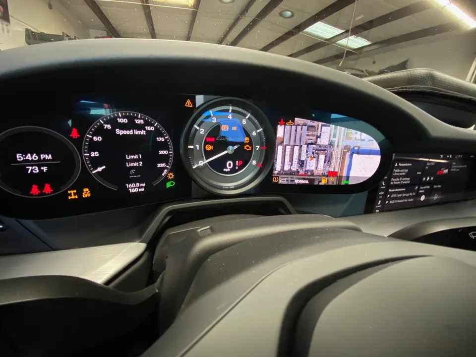 Close-up of a Porsche digital dashboard displaying speed, navigation, and various warning lights.