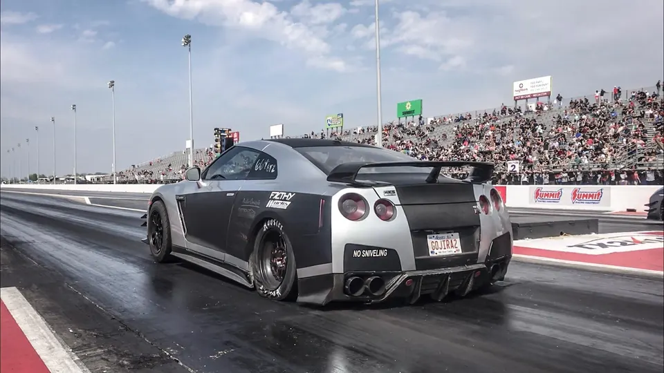 Silver and black Nissan GT-R with a widebody kit on a drag strip, preparing for a race with spectators in the background.
