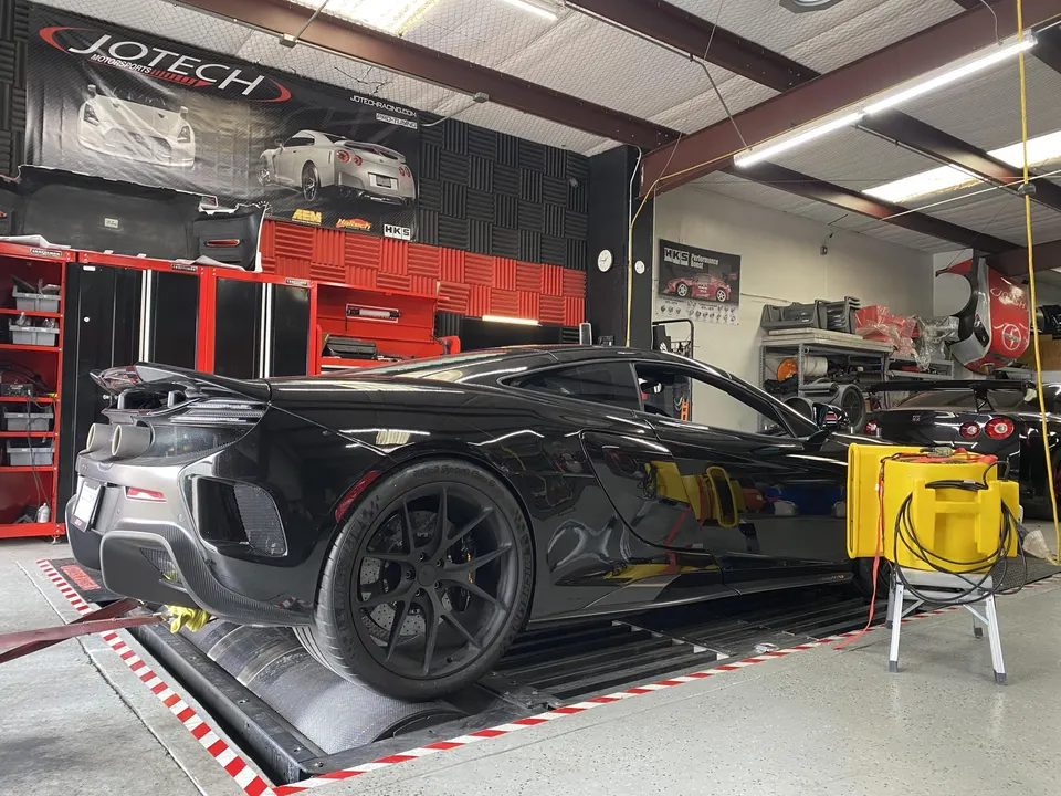 Black McLaren supercar strapped to a dynamometer at Jotech Motorsports for performance tuning and testing.