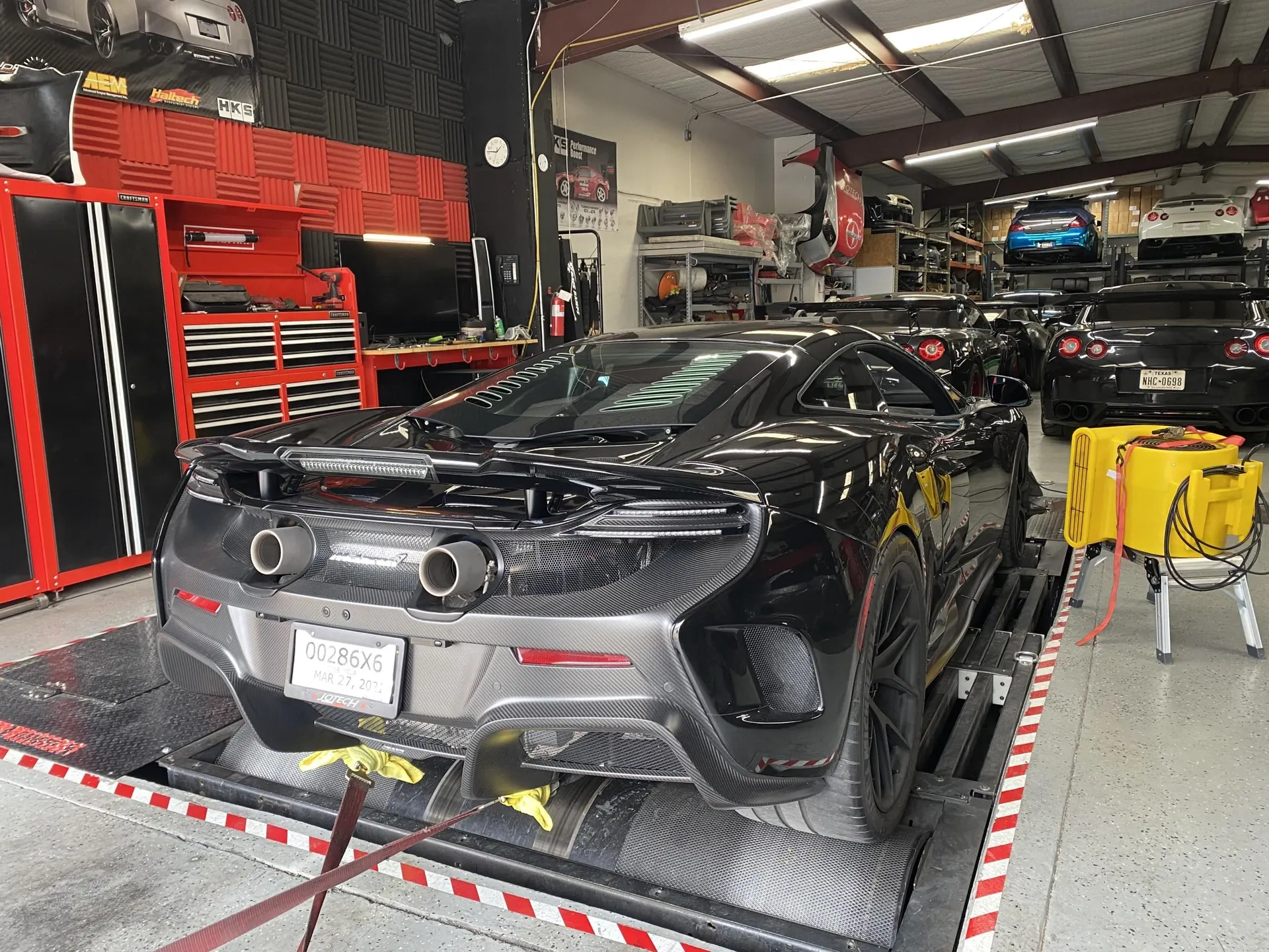Black McLaren 650S on a dyno at Jotech Motorsports shop, with other GT-Rs in the background.