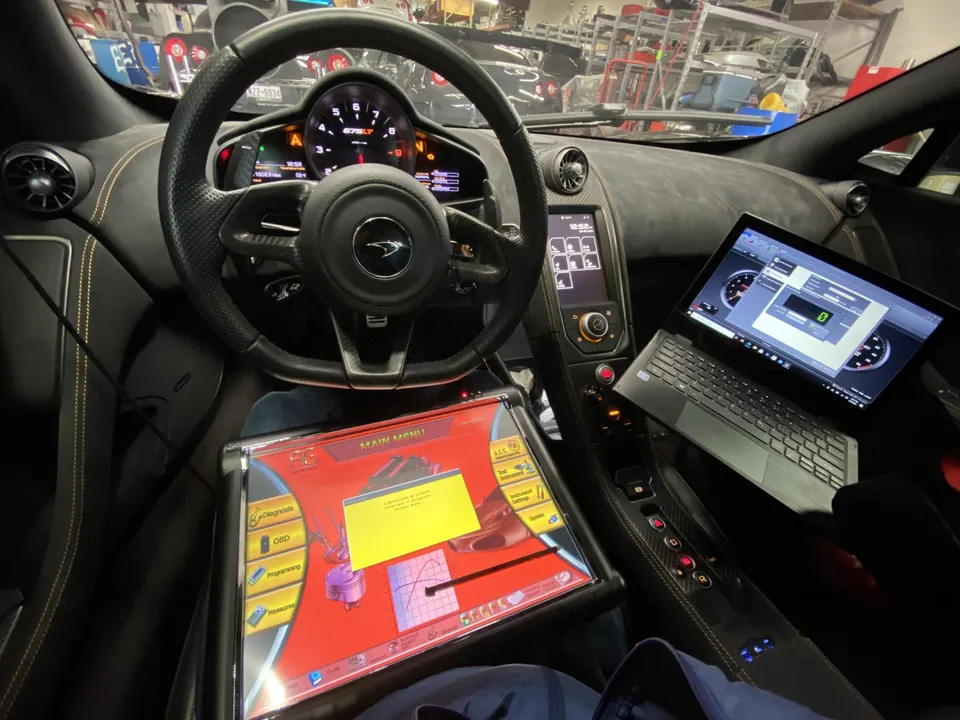 Interior view of a McLaren with a laptop and diagnostic tool connected for performance tuning.