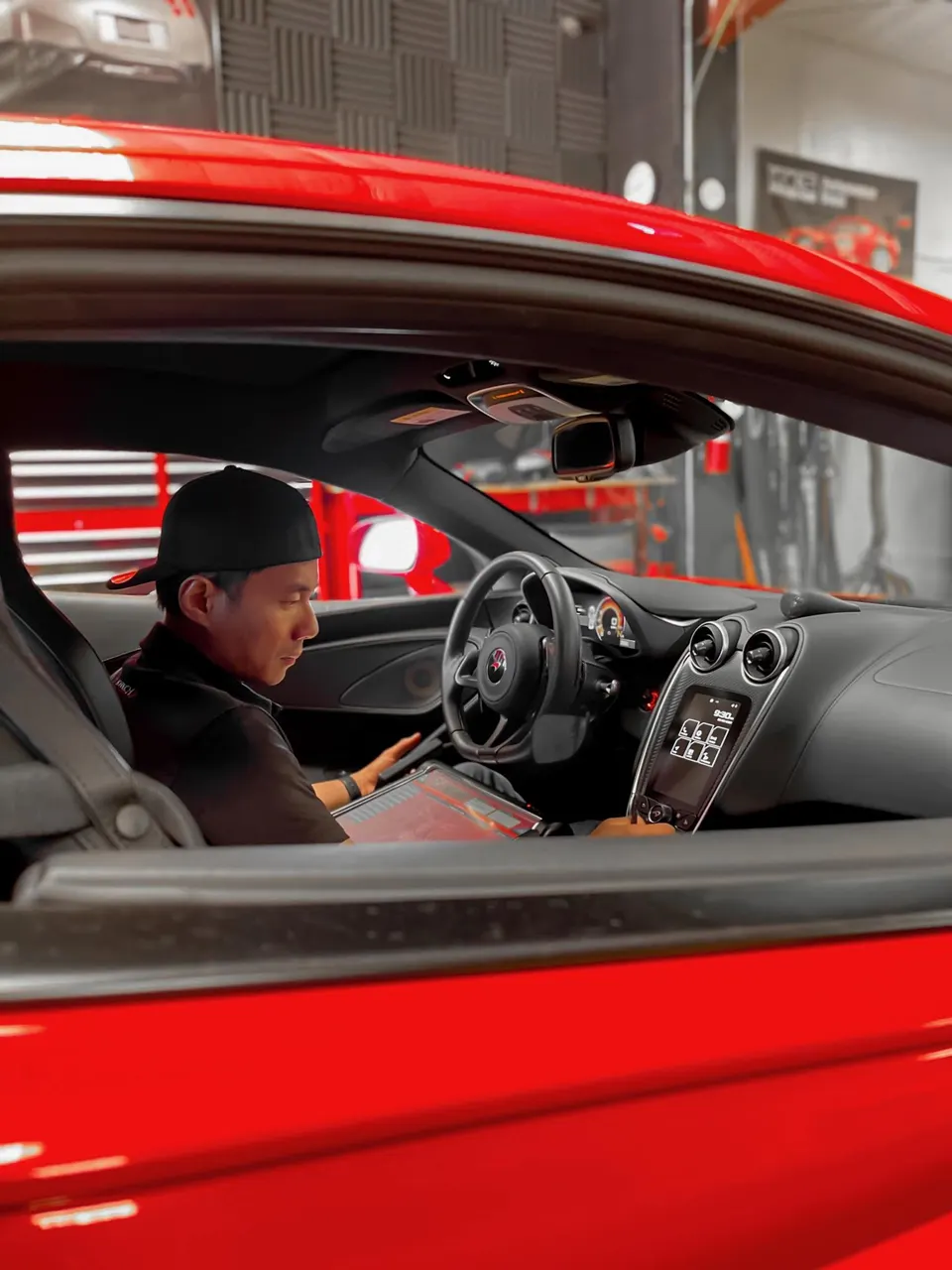 A person in a red McLaren working on the car's electronics with a tablet in a performance shop.
