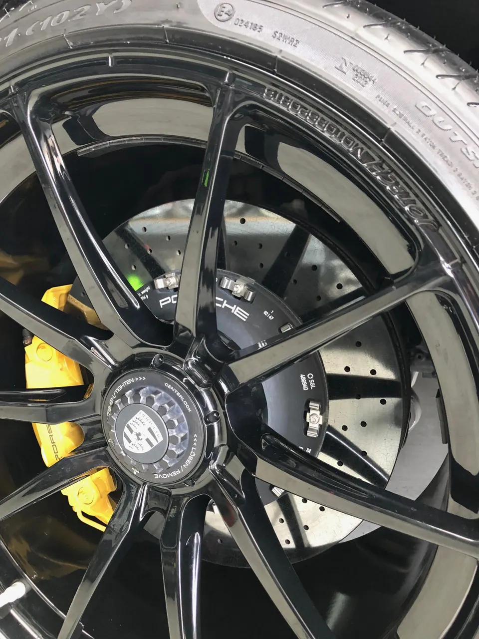 A close-up of a Porsche wheel with black spokes, yellow brake calipers, and a centerlock hub.