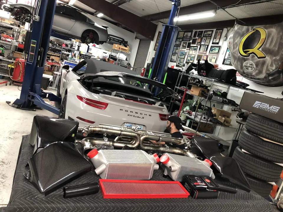 A Porsche 911 Turbo S in a performance shop with aftermarket intercoolers, exhaust, and carbon fiber intake parts.