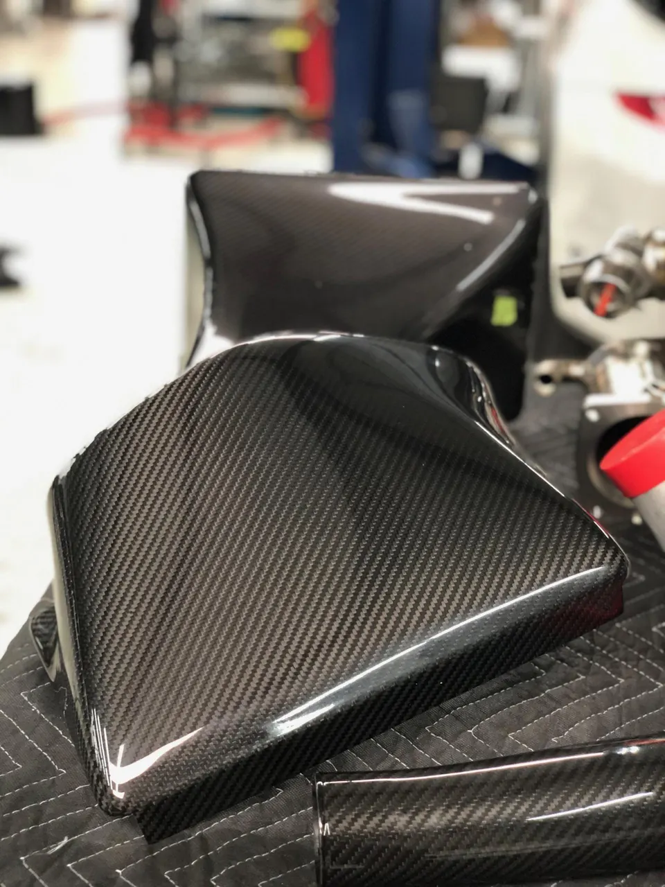 Close-up of multiple glossy carbon fiber automotive parts on a quilted mat, likely engine bay covers or exterior trim.