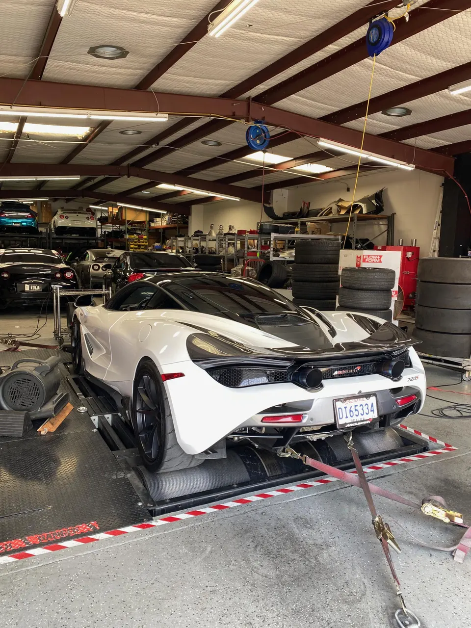 White McLaren 720S strapped to a dynamometer in a performance tuning shop, ready for a power run.