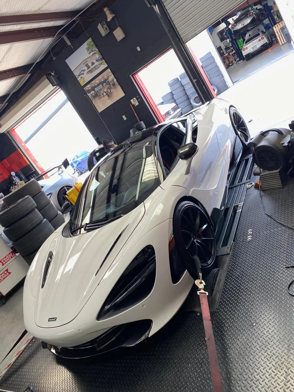 A white McLaren 720S supercar strapped to a dynamometer in a performance tuning shop, ready for power testing.