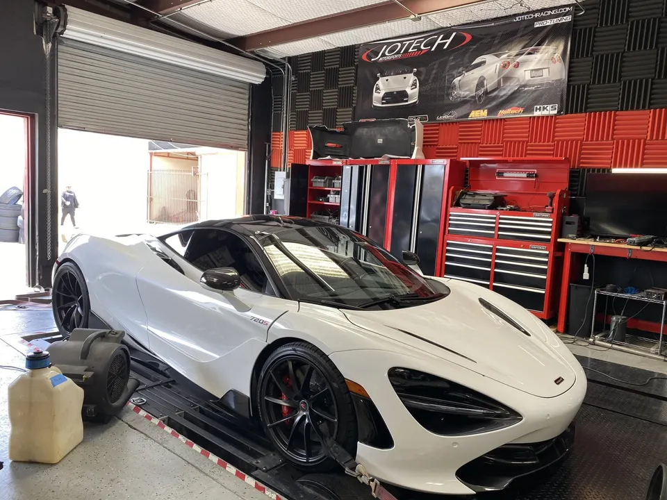 White McLaren 720S supercar strapped to a dynamometer at a performance tuning shop for power testing and calibration.
