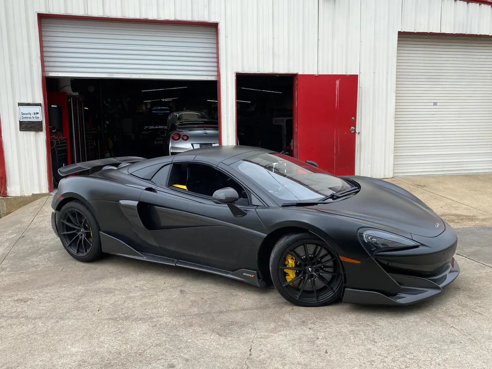Matte black McLaren 570S parked outside a Jotech Motorsports shop bay with a Nissan GT-R visible inside.