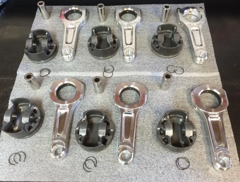 Forged pistons and connecting rods laid out for a high-performance engine build at a tuning shop.
