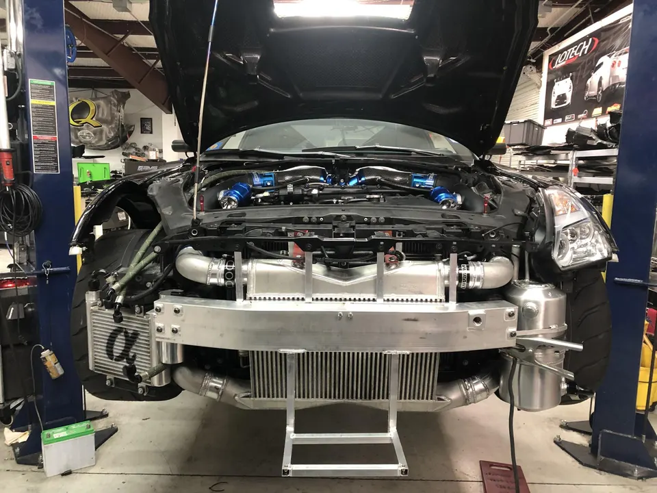 Front view of a Nissan 350Z on a lift in a shop, with the bumper removed revealing large intercoolers and boost piping.