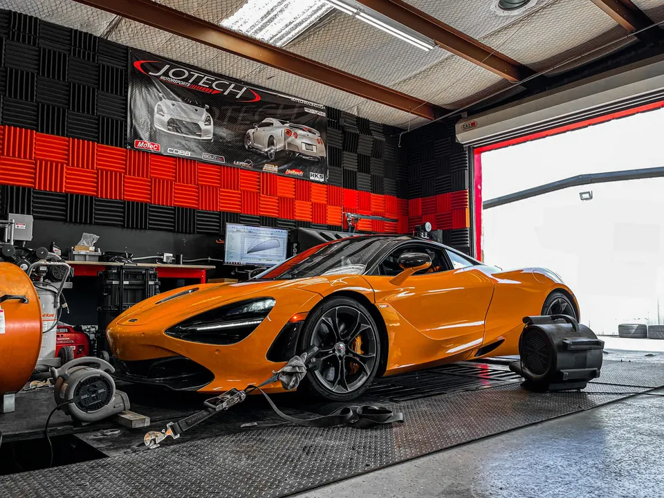 An orange McLaren 720S strapped to a dynamometer at Jotech Motorsports for performance tuning.
