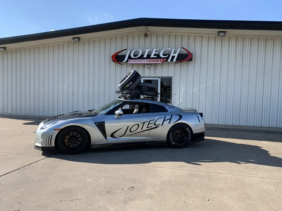 Silver Nissan GT-R with Jotech Motorsports livery and roof rack, parked outside Jotech Motorsports shop.
