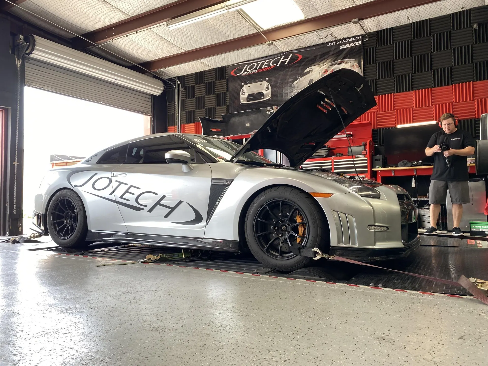 Silver Nissan GT-R R35 strapped to a dynamometer at Jotech Motorsports for performance tuning.