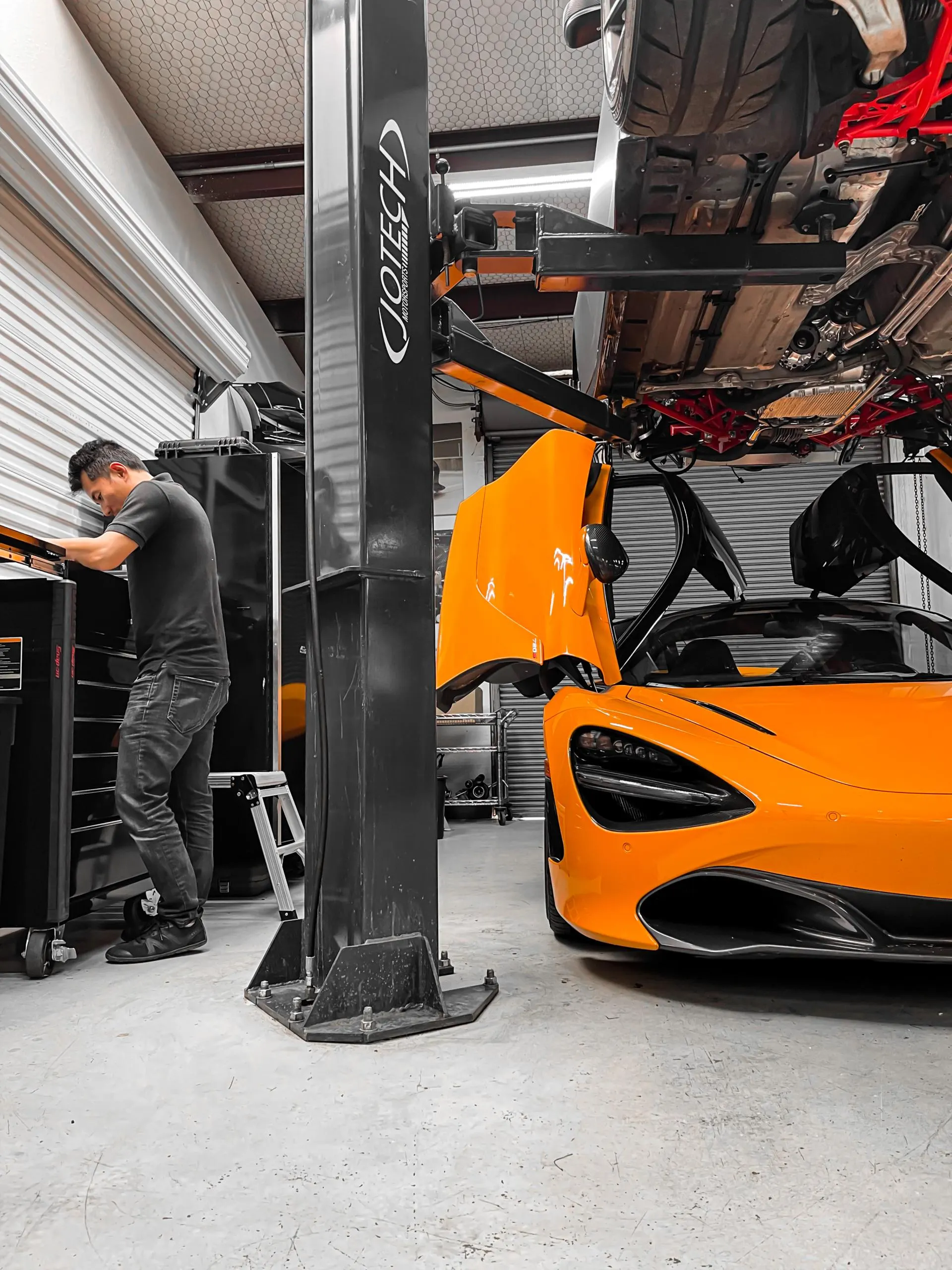 Mechanic working in the Jotech Motorsports shop with an orange McLaren and another car on a lift.