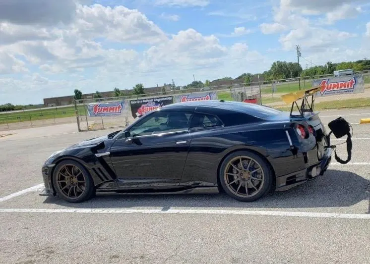 Black Nissan GT-R drag car with a large rear wing and parachute system parked at a track with Summit Racing banners.