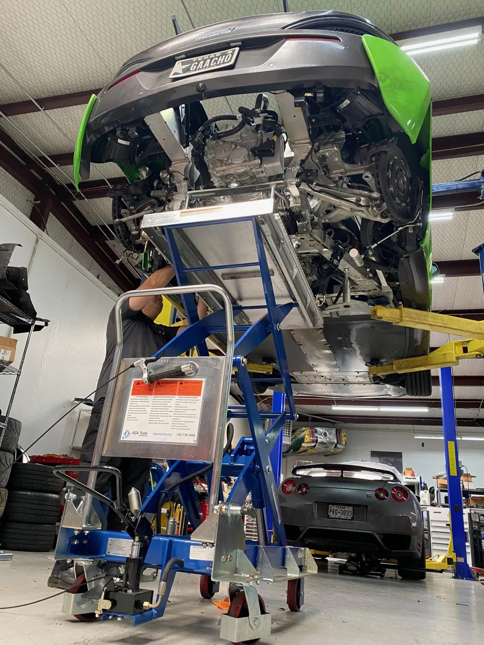 A McLaren supercar on a lift in a performance shop with its rear section removed, exposing the engine and drivetrain. A Nissan GT-R is in the background.