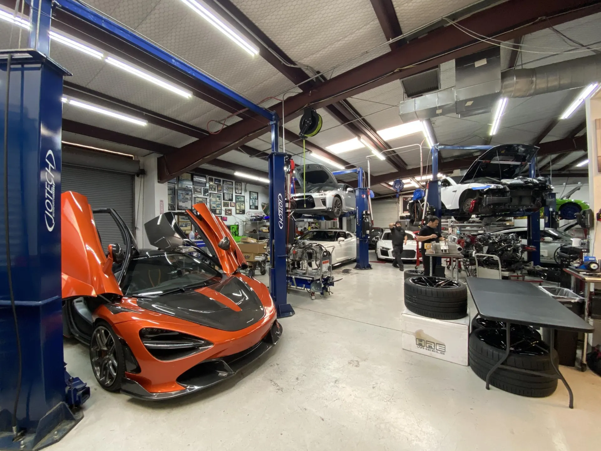 A wide shot of the Jotech Motorsports performance tuning shop with multiple high-performance cars on lifts and mechanics working.