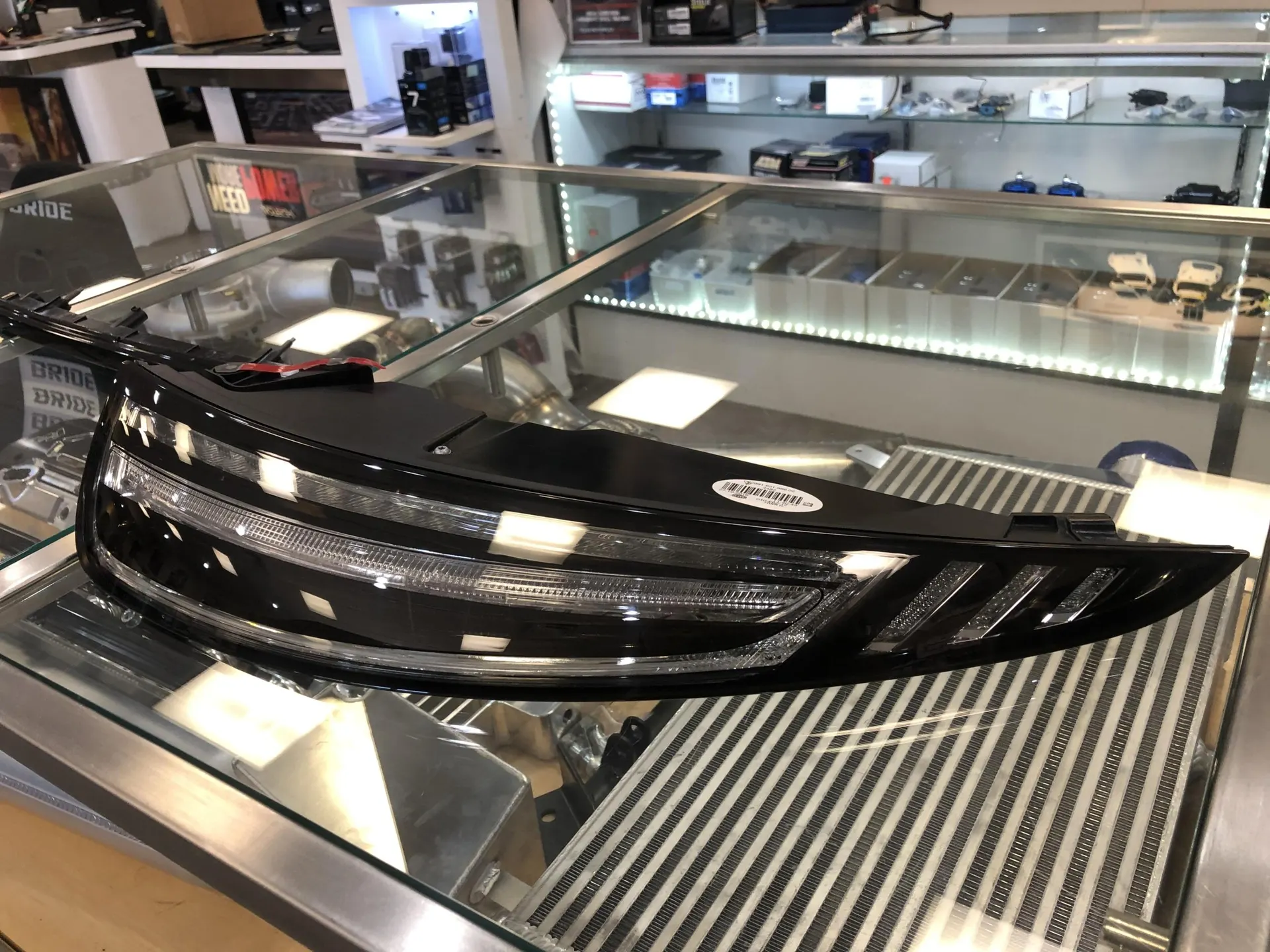 Aftermarket car headlight displayed on a glass case in a performance shop.
